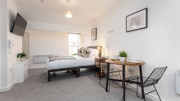 A modern bedroom with a bed, bedside table, and a small dining area with chairs and a table.