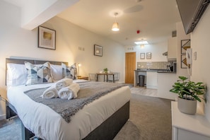 Une chambre d’hôtel moderne dotée d’un grand lit, d’une petite table à manger, d’une kitchenette et d’une salle de bain.