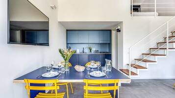 Ein moderner Essbereich mit einem dunkelblauen Tisch und gelben Stühlen, eine Küche mit blauen Schränken und eine Treppe mit Holzboden.