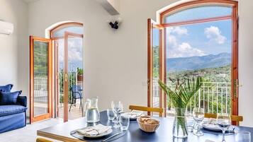 Ein Essbereich mit Tisch für vier Personen, große Fenster mit Blick auf die Berge und eine blaue Couch im Hintergrund.