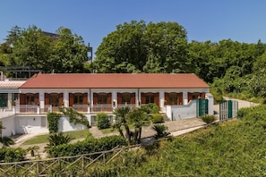 A two-story house with a red-tiled roof, white walls, and a balcony with a railing.