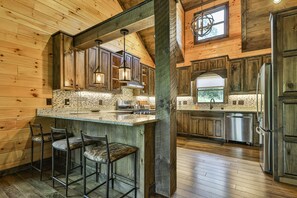 A rustic kitchen with wooden cabinets, a large island with bar stools, and a stainless steel refrigerator.