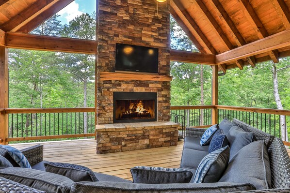 A covered outdoor seating area with a stone fireplace and a flat-screen TV mounted above it.