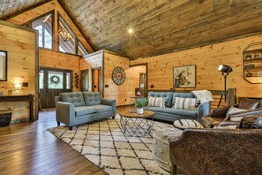 A cozy log cabin interior with a wooden ceiling, a large clock, and a fireplace.