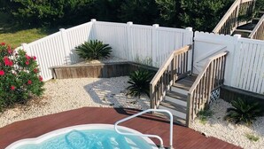 A swimming pool with a wooden deck, a white fence, and a staircase leading to a deck area.