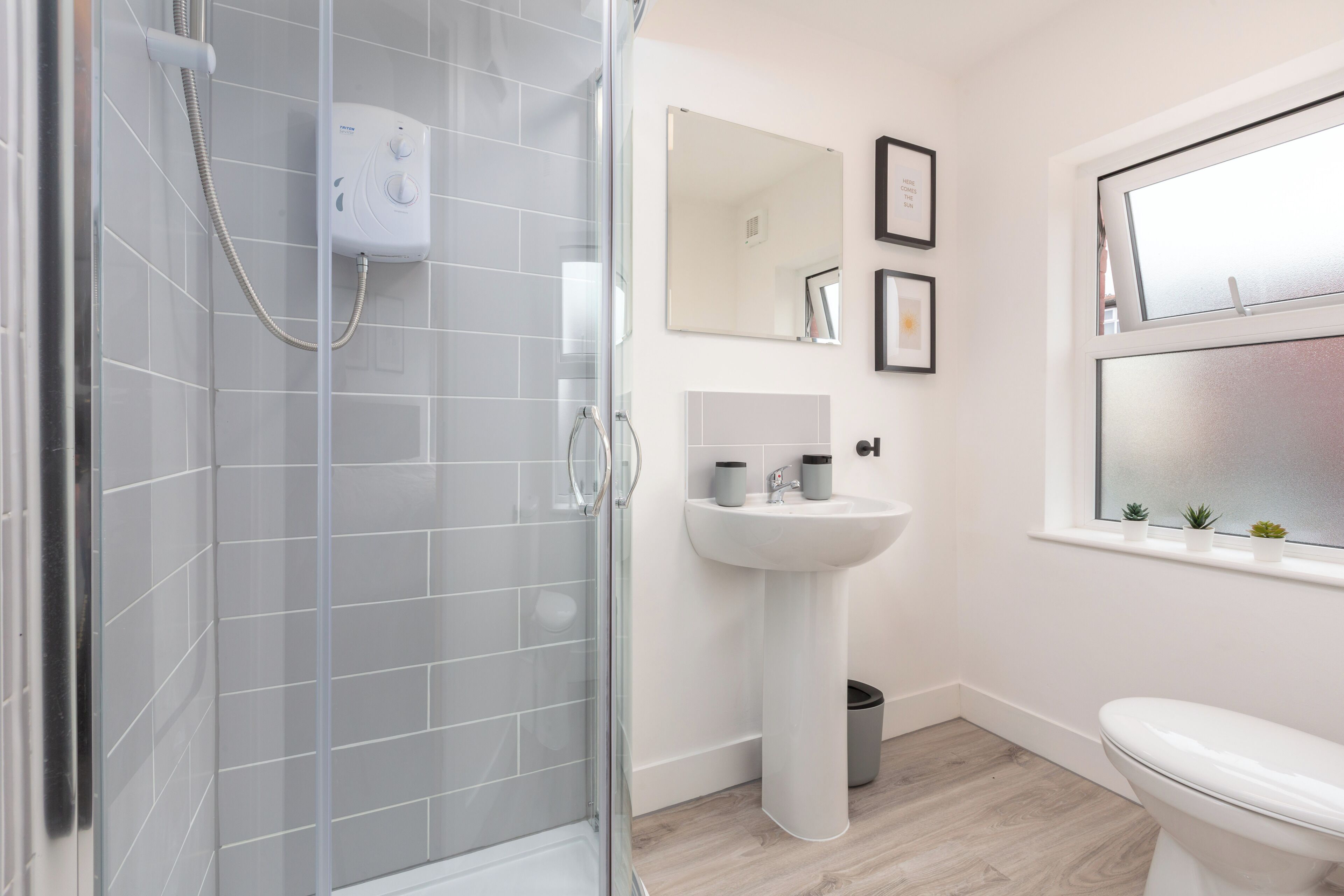 Un baño moderno con cabina de ducha de vidrio, lavabo pedestal y inodoro.