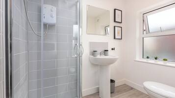 Un baño moderno con cabina de ducha de vidrio, lavabo pedestal y inodoro.