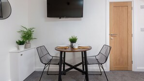 Una habitación con un televisor en la pared, una puerta de madera, un armario blanco, dos sillas, una mesa con una planta y una maceta sobre el mueble.