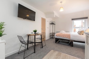 Ein modernes Hotelzimmer mit Bett, Wandfernseher, kleinem Esstisch mit Stühlen, Zimmerpflanze und Fenster mit Blick.