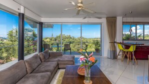 A modern living room with a large sectional sofa, a dining area with yellow chairs, and a view of greenery through large windows. - Villa Mar y Sol: 4 Independent Apartments in Quiet, Natural Area w/ wildlife! (Manuel Antonio)