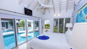 A hotel room with a large bed, a view of a swimming pool, and a ceiling fan. - Turtle Breeze - Fully Staffed Oceanfront Villa with Private Chef (Turtle Cove)