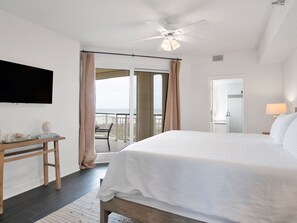 Ein Schlafzimmer mit Bett, Schreibtisch, Fernseher, Deckenventilator und Meerblick vom Balkon.