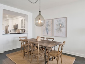 A dining area with a wooden table and chairs, a hanging pendant light, and two framed artworks on the wall.