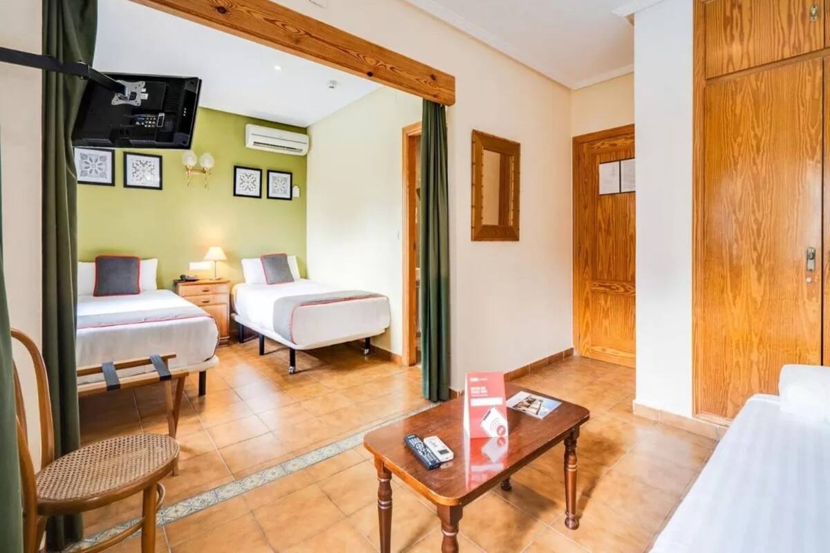 Une chambre d’hôtel avec deux lits, une table en bois, une chaise, un téléviseur et une armoire.