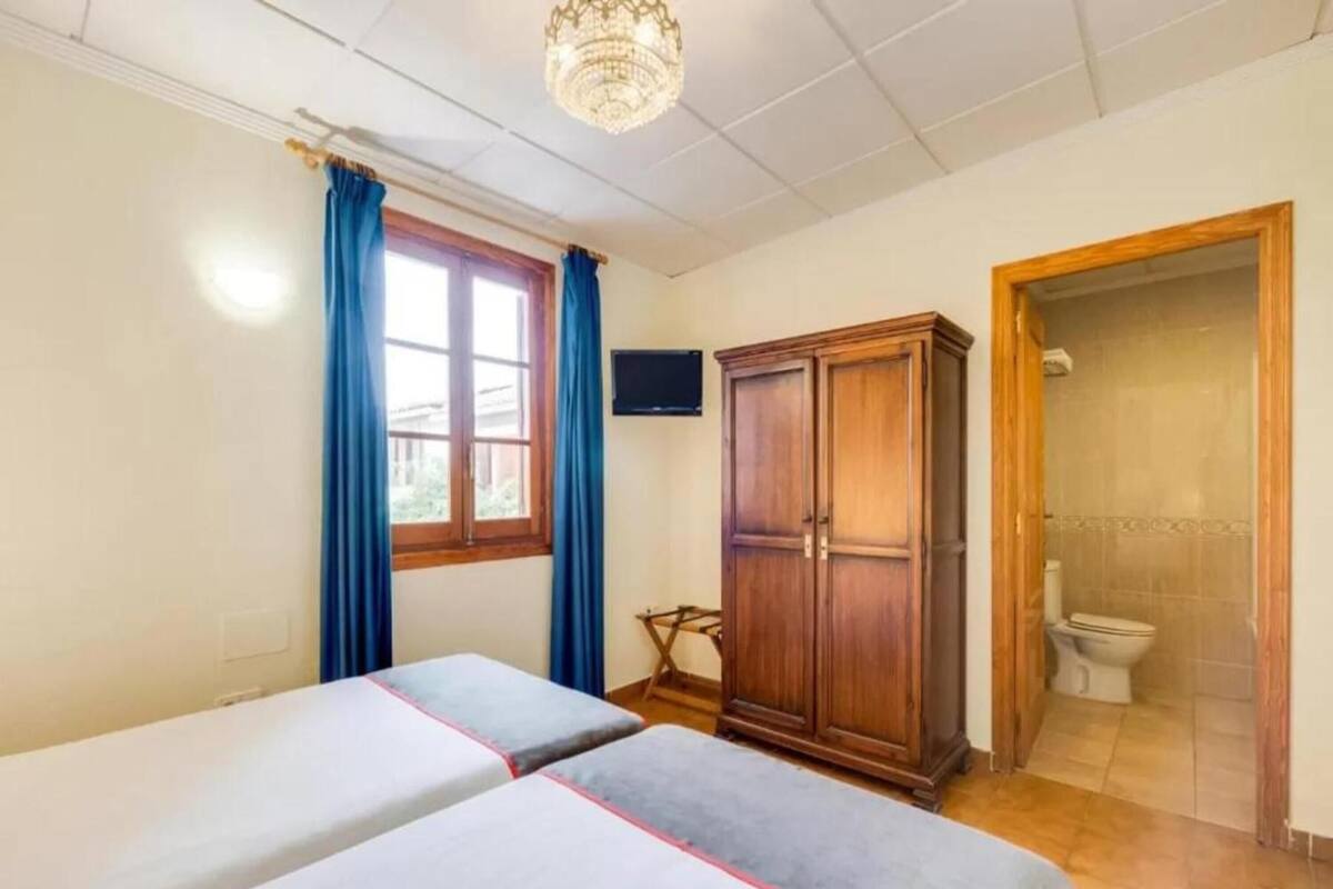Une chambre avec deux lits, une armoire en bois, une télévision et une salle de bain avec des toilettes.