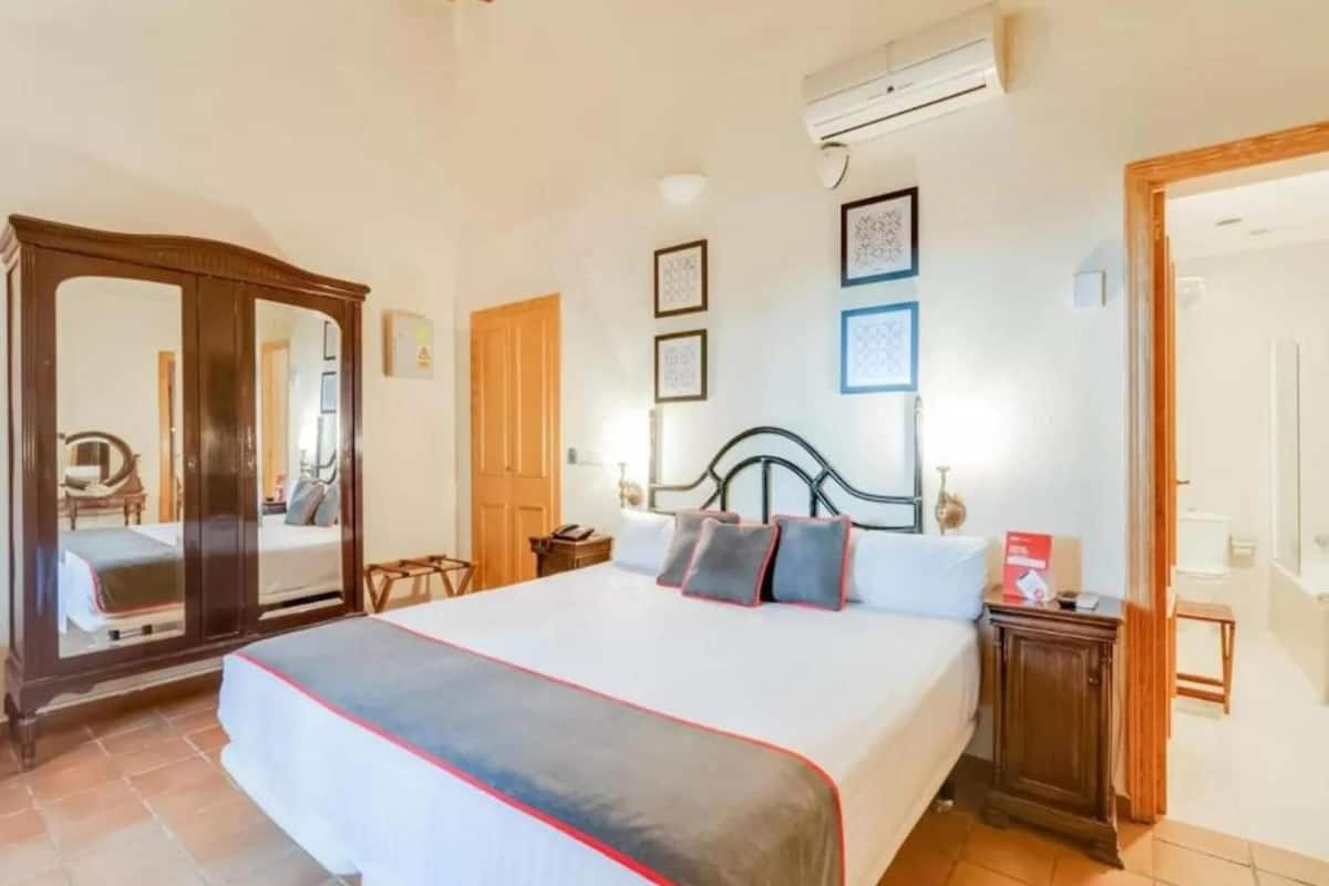 Une chambre d’hôtel avec un grand lit, une armoire en bois et une petite table de chevet.