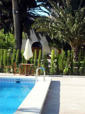 A swimming pool with a geometric tile pattern, surrounded by palm trees and a white umbrella. - Hotel Torre San Juan (San Juan de Alicante)