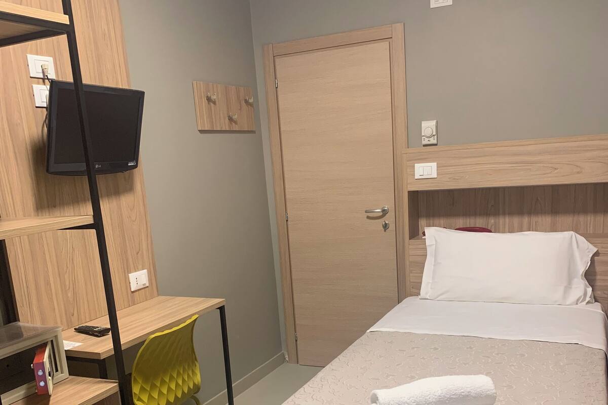 A hotel room with a bed, a desk, a chair, a wardrobe, and a television.