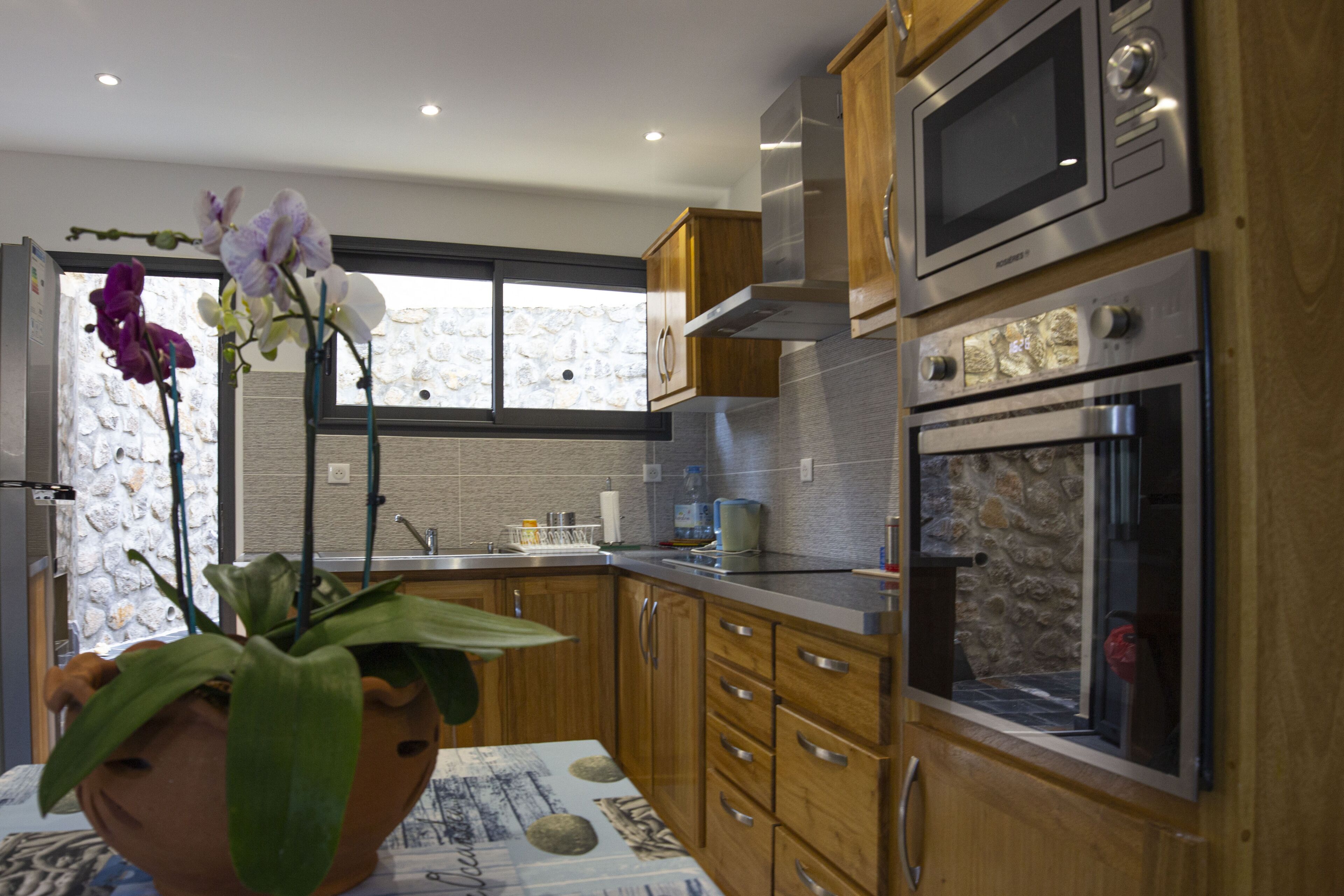 Een moderne keuken met houten kastjes, roestvrijstalen apparatuur en een groot raam met een stenen muur.