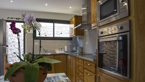 A modern kitchen with wooden cabinets, stainless steel appliances, and a large window with a stone wall. - T2 - 66m2 - Résidence Georgette ☆☆☆☆ (SAINT-PIERRE)