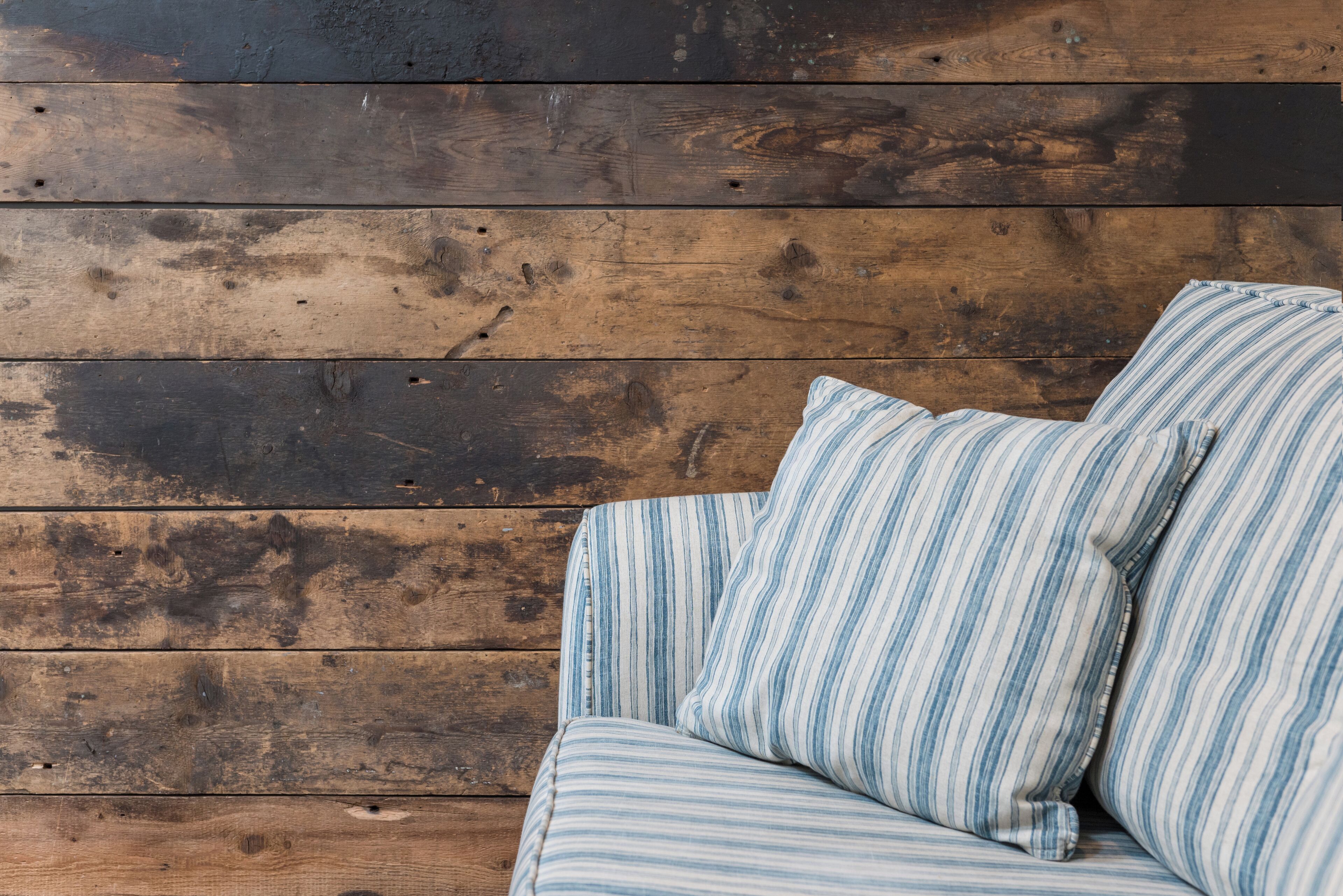 Eine Holzwand mit horizontalen Lamellen und ein gestreiftes Kissen auf einer Couch.
