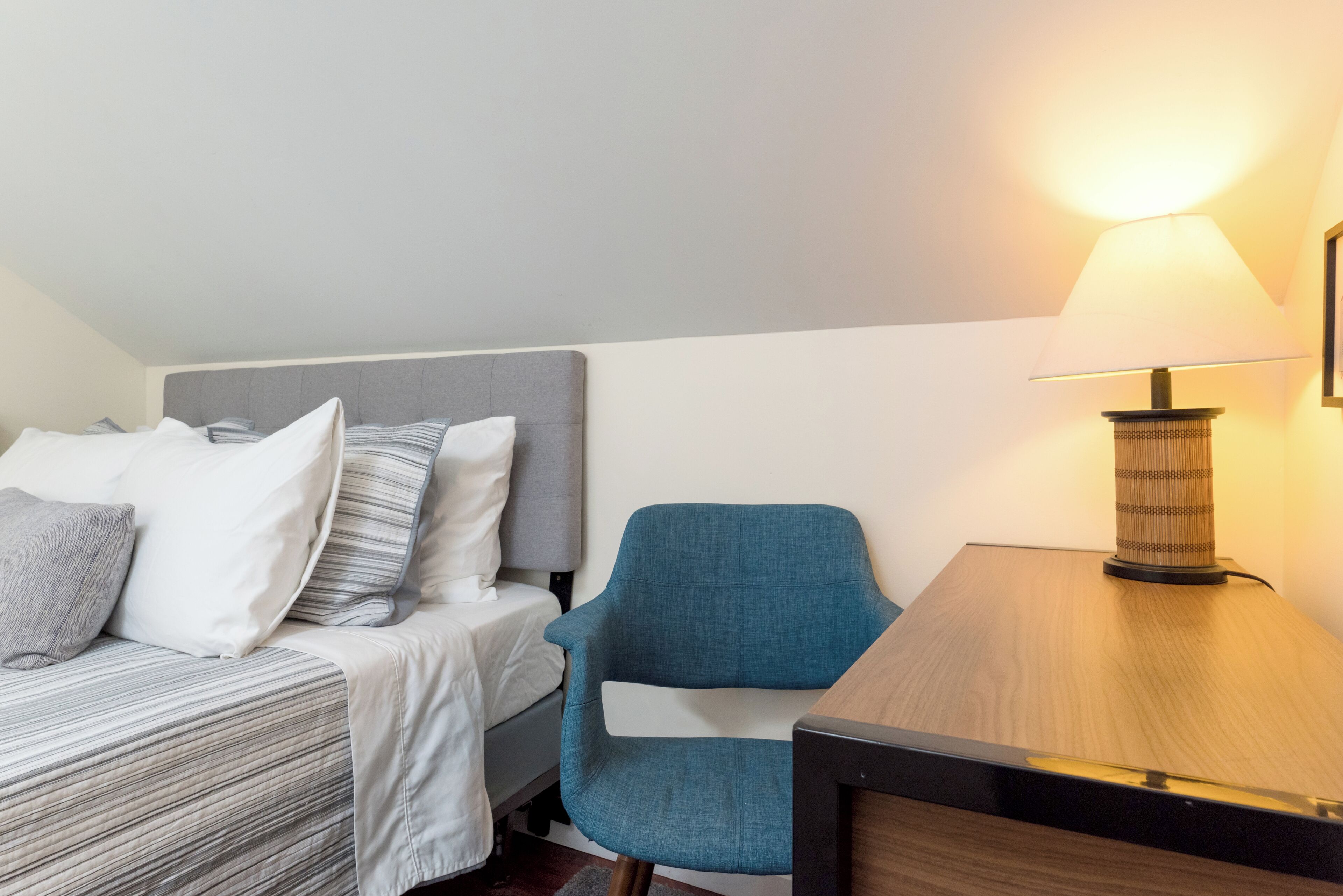 A hotel room with a bed, a chair, a table, and a lamp.