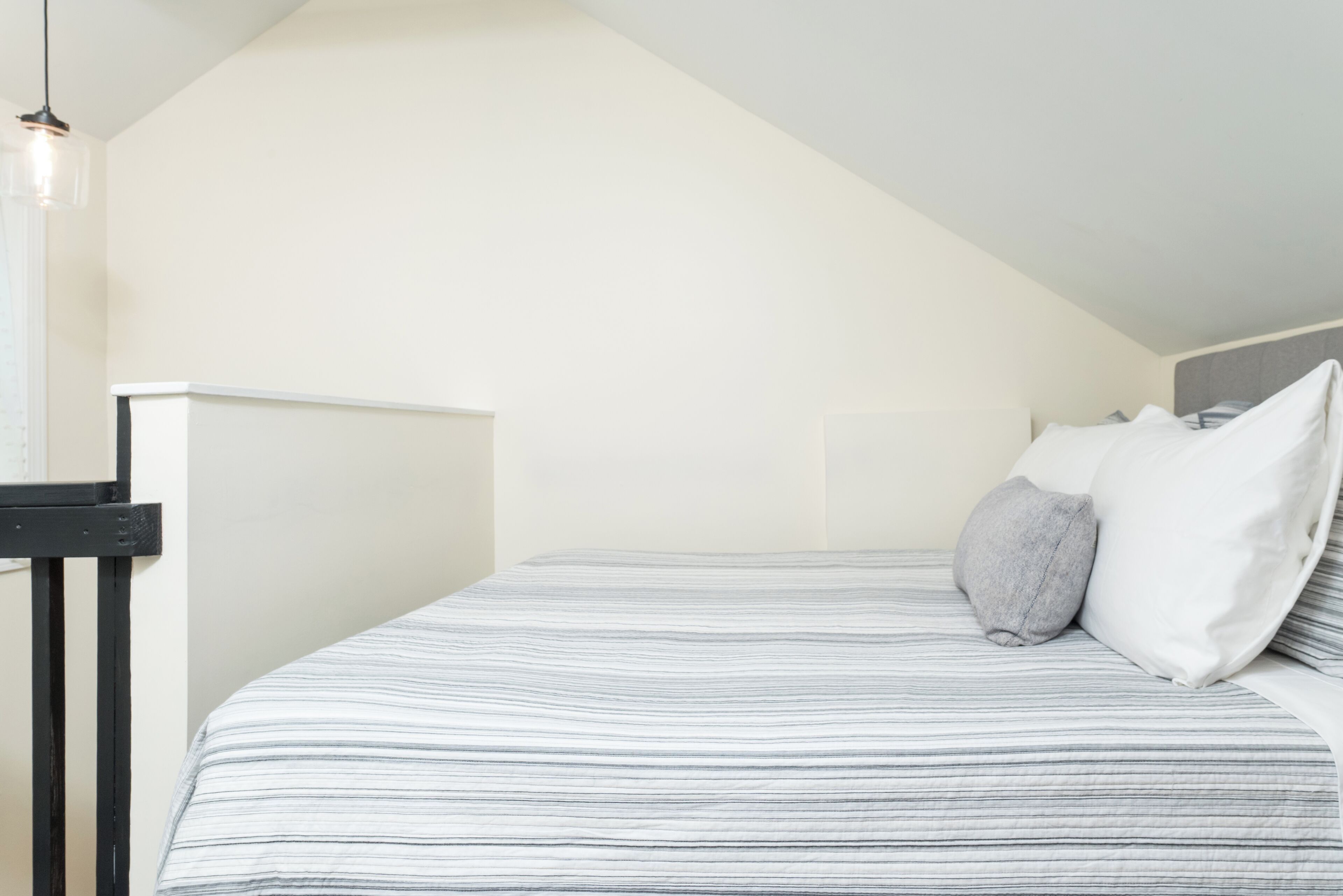 A bedroom with a sloped ceiling, a bed with striped bedding, a bedside table, and a hanging light fixture.