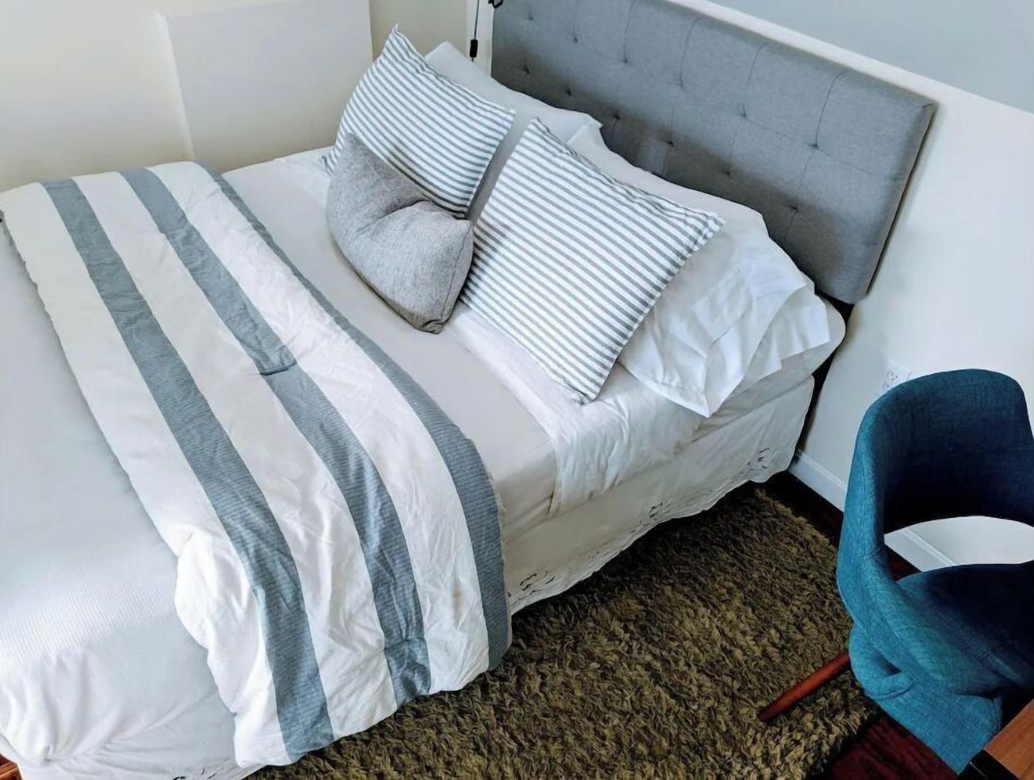 Ein ordentlich bezogenes Bett mit gestreifter Bettwäsche und einem grauen Kopfteil.