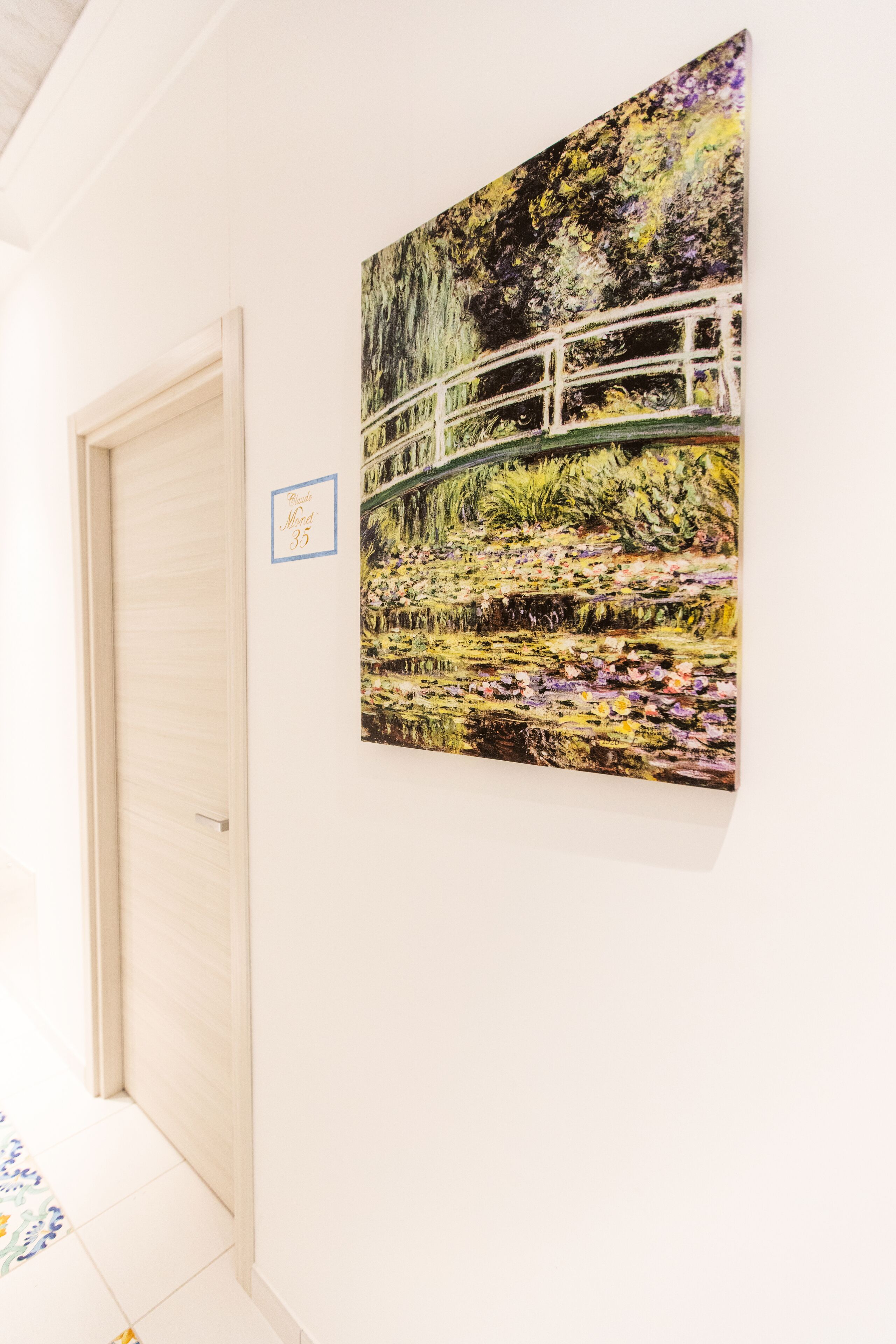 A hallway with a white door and a framed painting of a bridge over water.