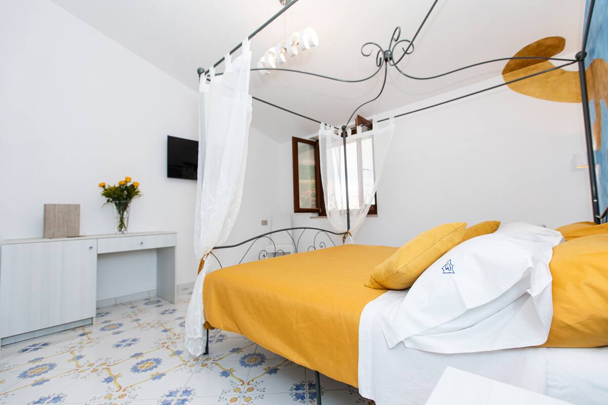 A bedroom with a bed, a bedside table, a mirror, and a wall-mounted TV.