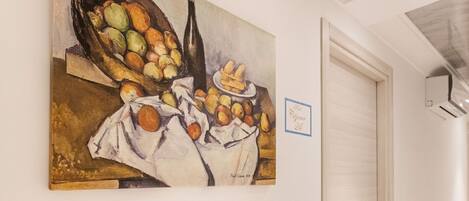 Un pasillo con un cuadro de frutas y verduras en la pared, una puerta cerrada y baldosas de suelo con diseños.