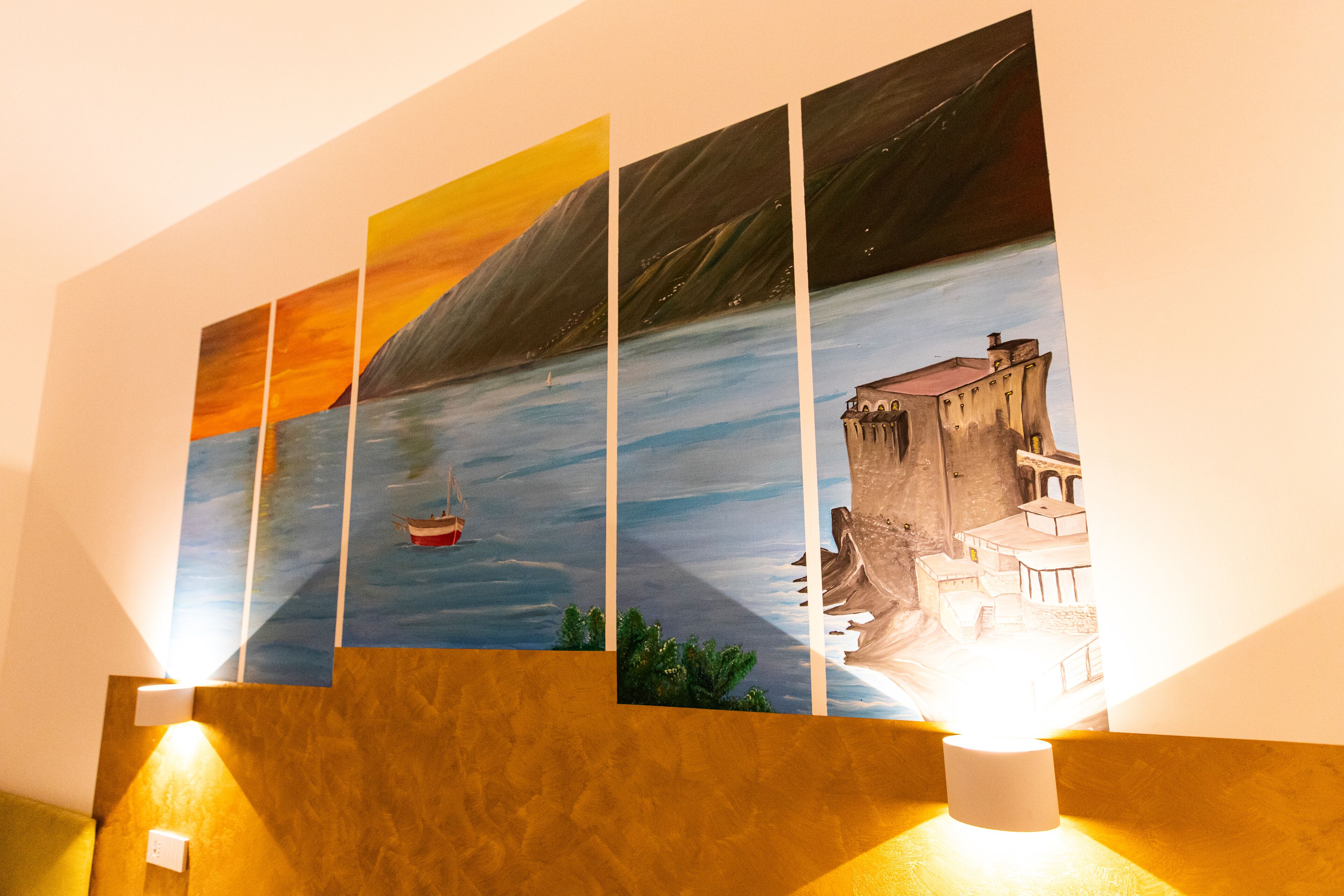 Pared con un cuadro de varios paneles que muestra una escena costera con un barco y un edificio.