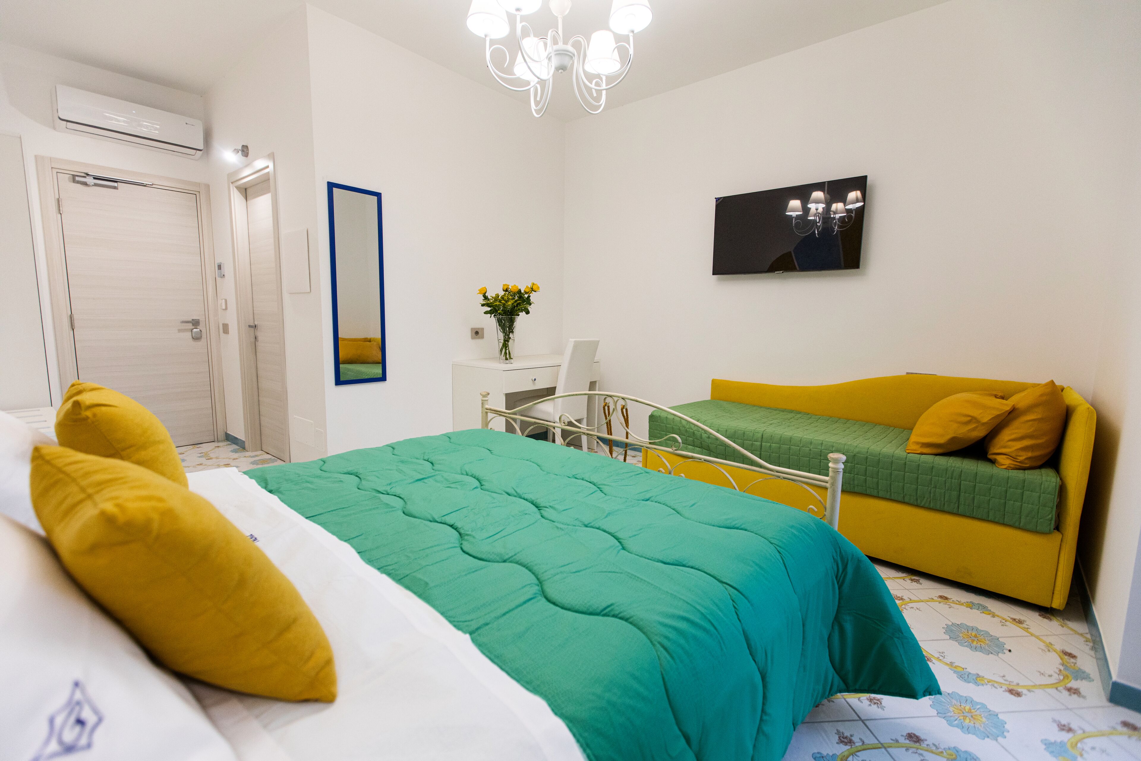 Un dormitorio con cama, sofá, espejo, televisor montado en la pared y unidad de aire acondicionado.