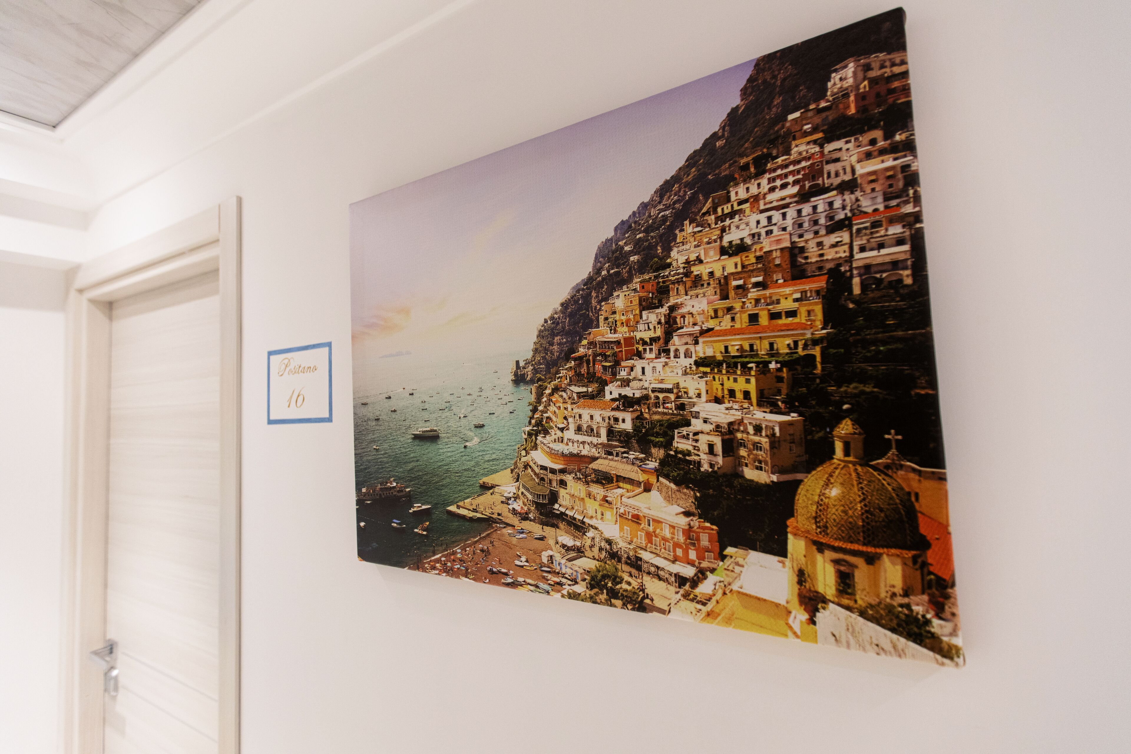 A hotel room with a large painting of a coastal town.