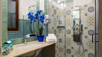 A bathroom with a sink, mirror, blue orchid plant, shower, and patterned tiles.