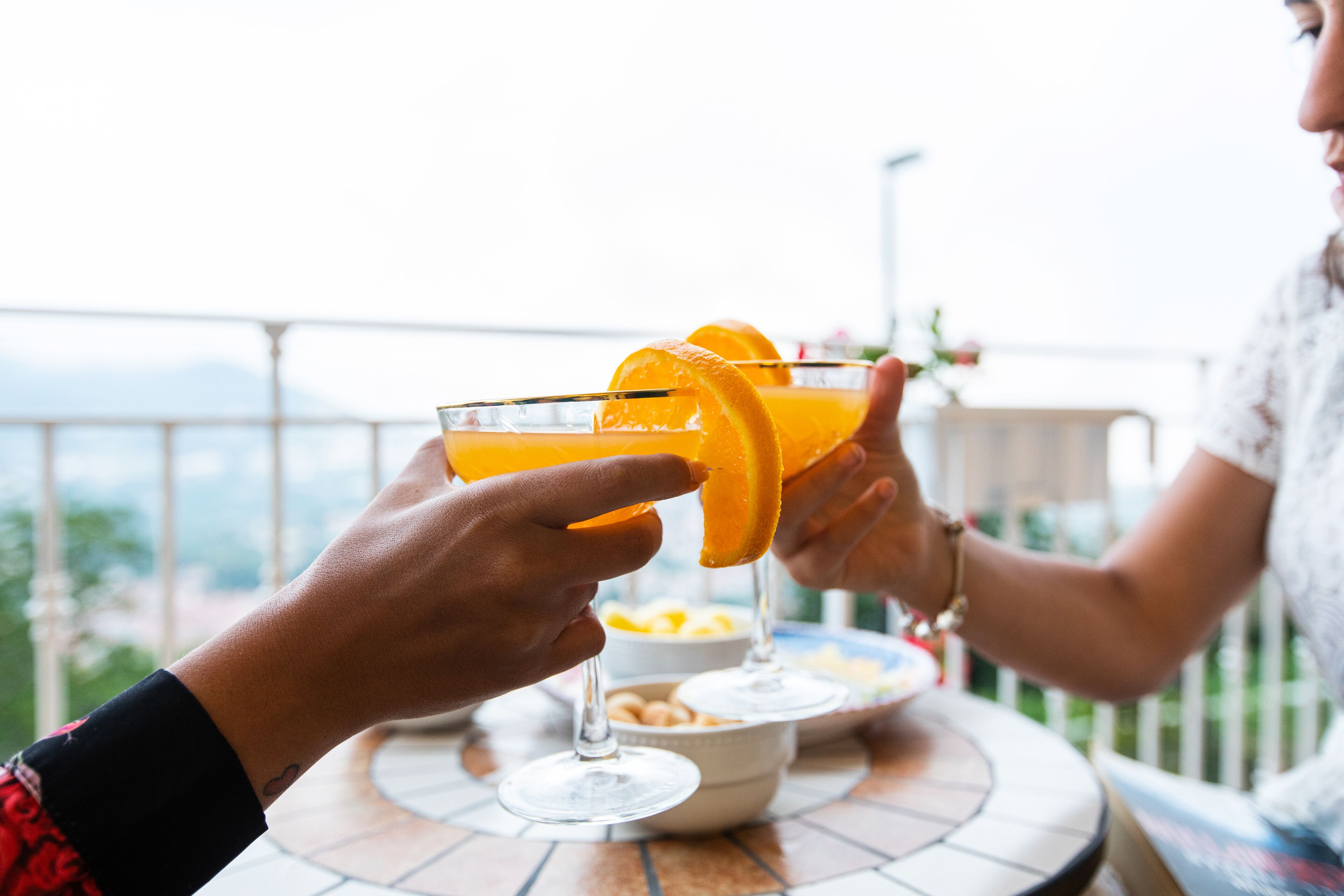 Two people toasting with orange drinks at a table with a bowl of snacks.