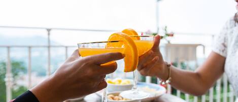 Two people toasting with orange drinks at a table with a bowl of snacks.