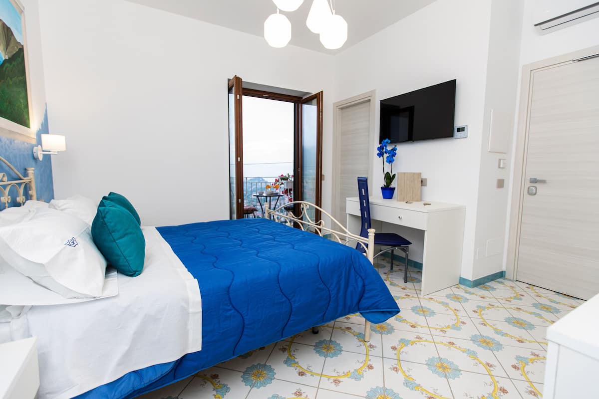 A bedroom with a bed, a desk, a chair, a TV, and a door.