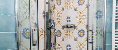 A shower area with glass doors, a showerhead, and a tiled wall with a floral pattern.
