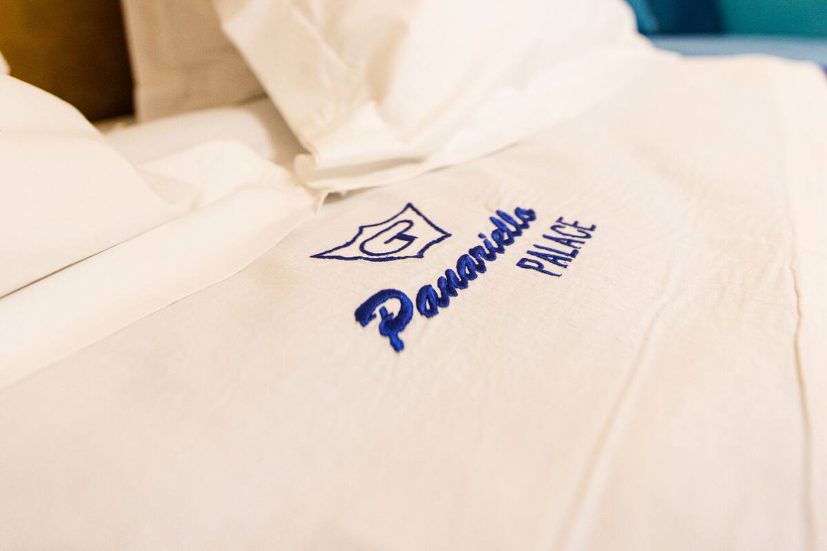A hotel bed with a white pillow and a white bedspread with a logo and text.