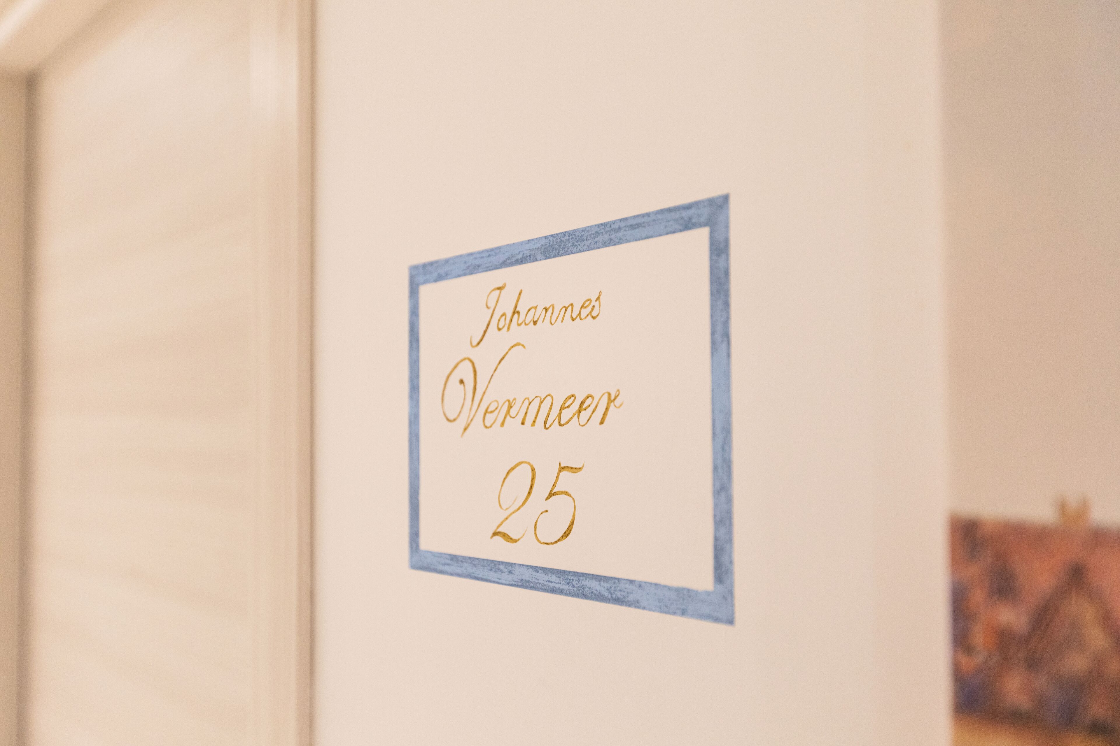 A wall with a framed sign that reads "Johannes Vermeer 25".