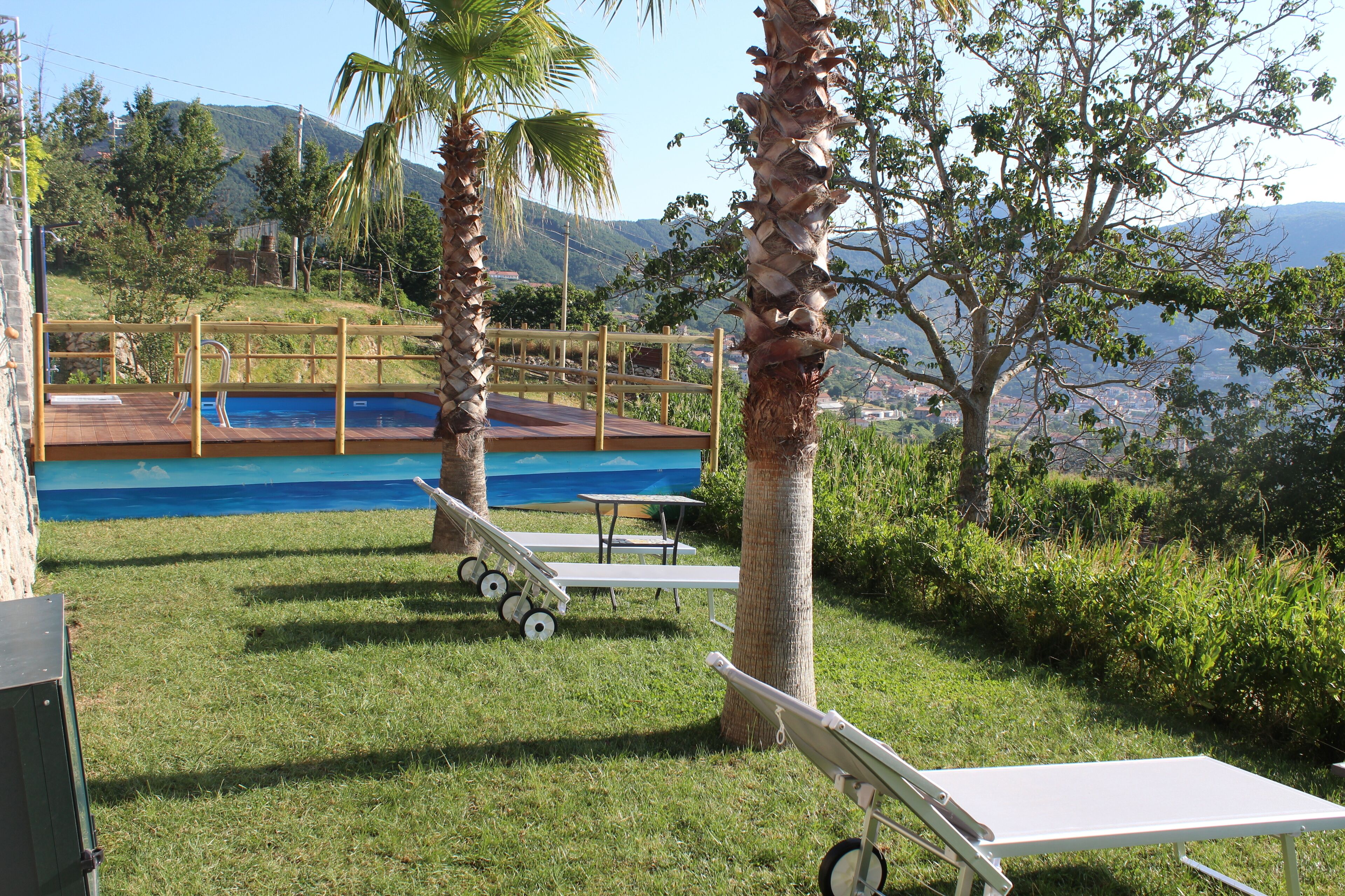 A pool area with a wooden deck, lounge chairs, and a view of mountains.
