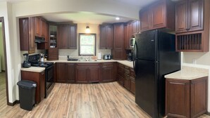 A kitchen with wooden cabinets, a black refrigerator, a microwave, and a stove. - Country Cottage Finger Lakes Region Destination Getaway (LaFayette)