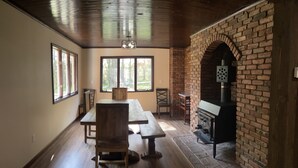 A dining area with wooden tables and chairs, large windows, and a brick fireplace. - Country Cottage Finger Lakes Region Destination Getaway (LaFayette)