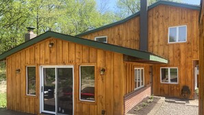 A wooden cabin with a deck, large sliding glass doors, and a brick pathway leading to a garden area. - Country Cottage Finger Lakes Region Destination Getaway (LaFayette)