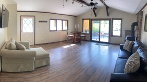 A spacious living room with a wooden floor, a sofa, a chair, a dining table, and a fireplace. - Country Cottage Finger Lakes Region Destination Getaway (LaFayette)