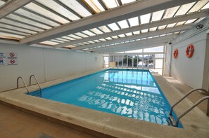 En inomhuspool med klart vatten, metallstegar och säkerhetsskyltar på väggarna.