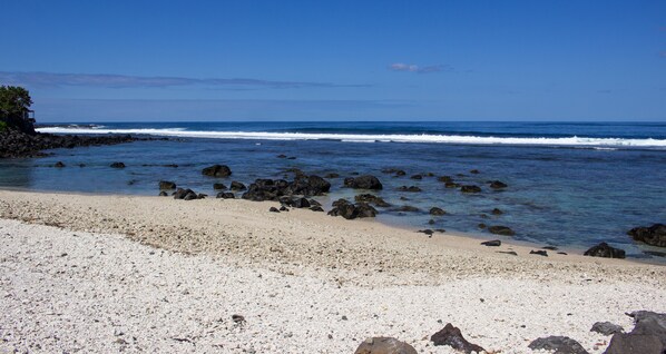 A beach with pebbly shore, clear blue water, and scattered rocks.