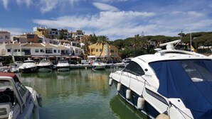 Un puerto deportivo con varias embarcaciones amarradas, rodeado de edificios y palmeras.