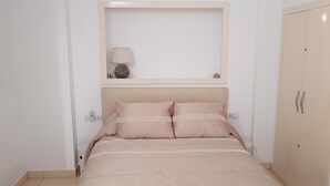 Un dormitorio con una cama, lámparas de noche, un estante en la pared con una lámpara y un armario.